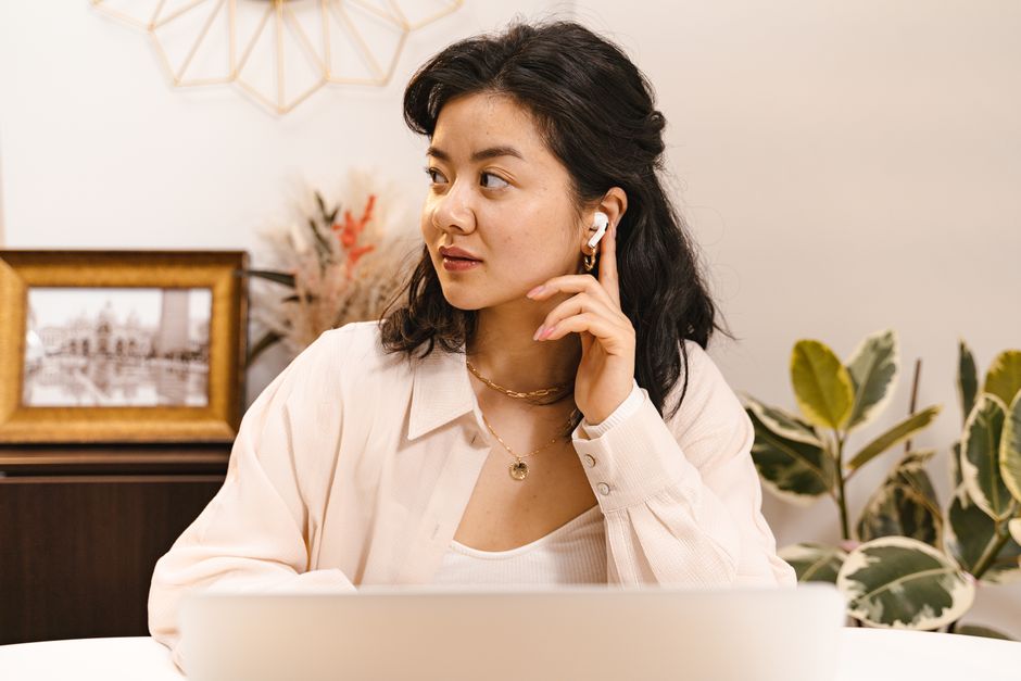 Asian woman with AirPods listening attentively while sitting indoors and wearing a gold necklace.